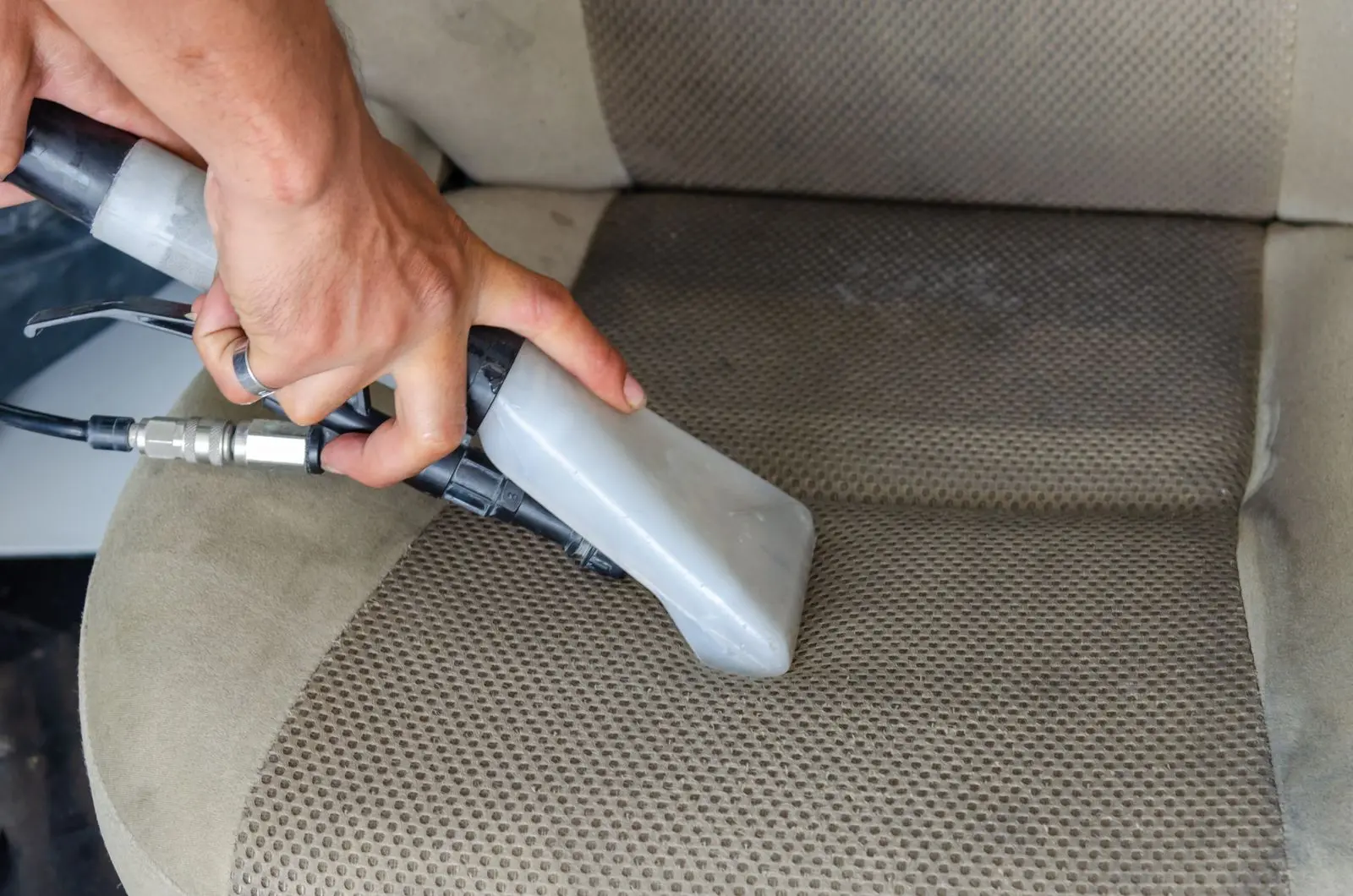 An upholstery extraction tool lifting moisture from a woven fabric car seat.