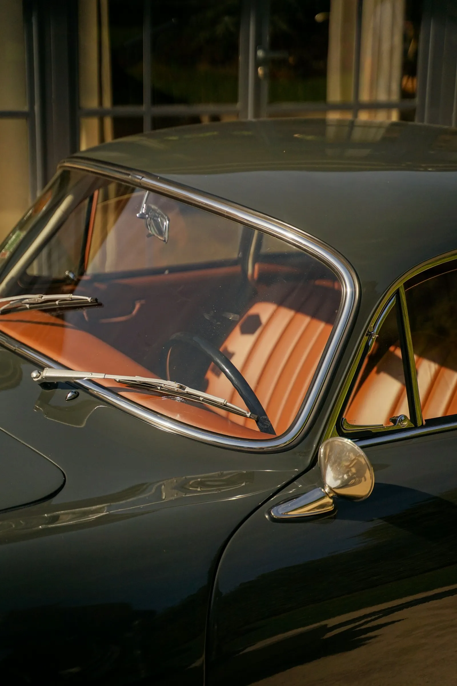 Warm brown leather upholstery and the steering wheel inside a vintage car, seen through its window.