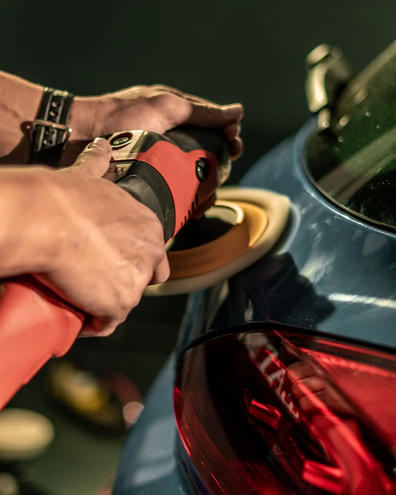 Hands guiding a machine polisher over the rear quarter panel of a car.