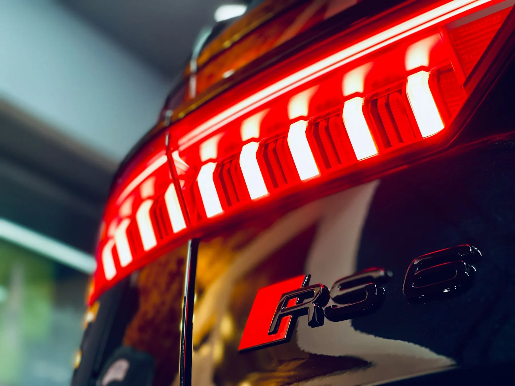 Monochrome close-up of an Audi tail light, with repeated illuminated segments and reflections across the bodywork.
