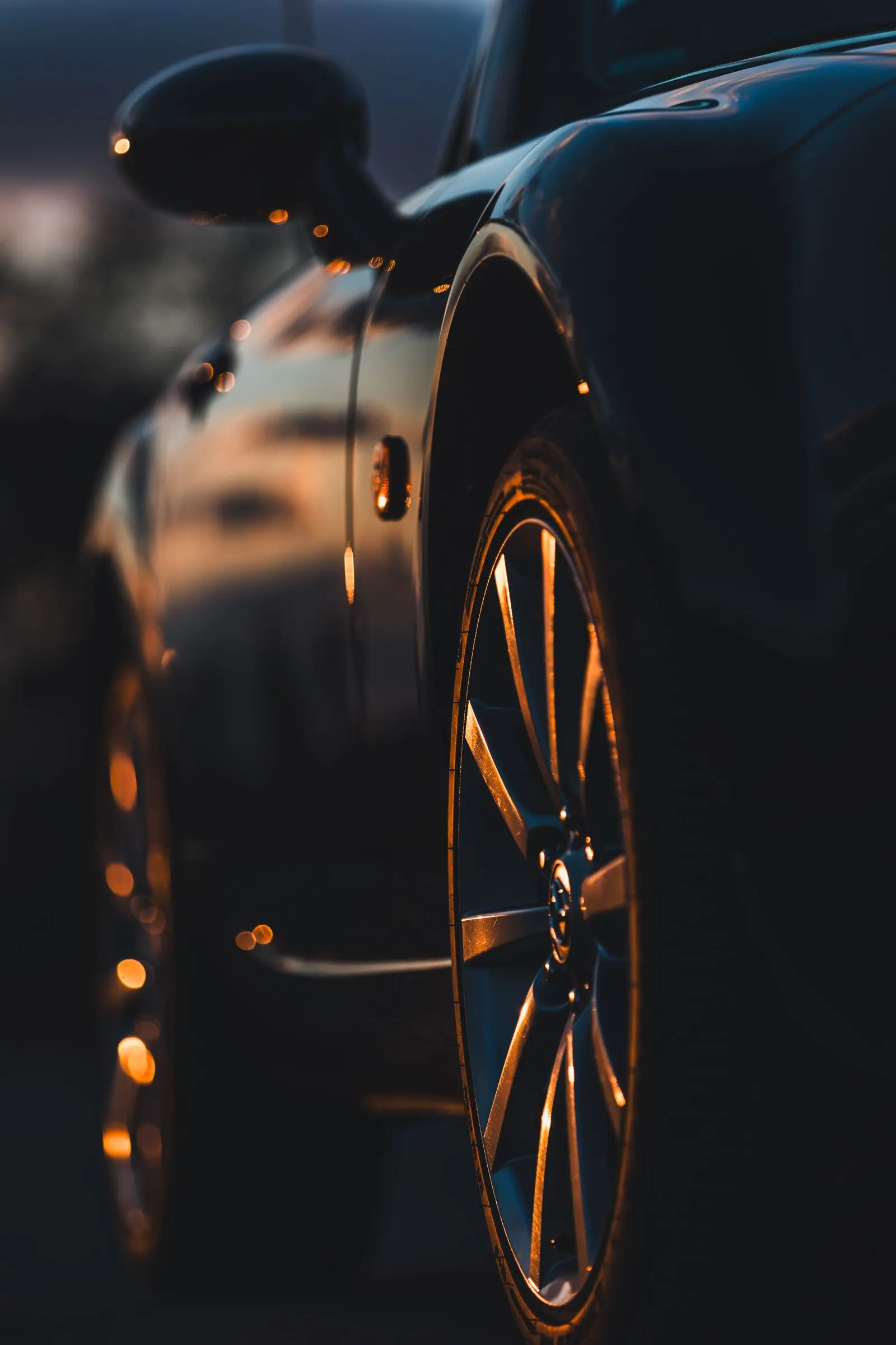 Warm evening reflections tracing a dark wheel arch and alloy wheel.