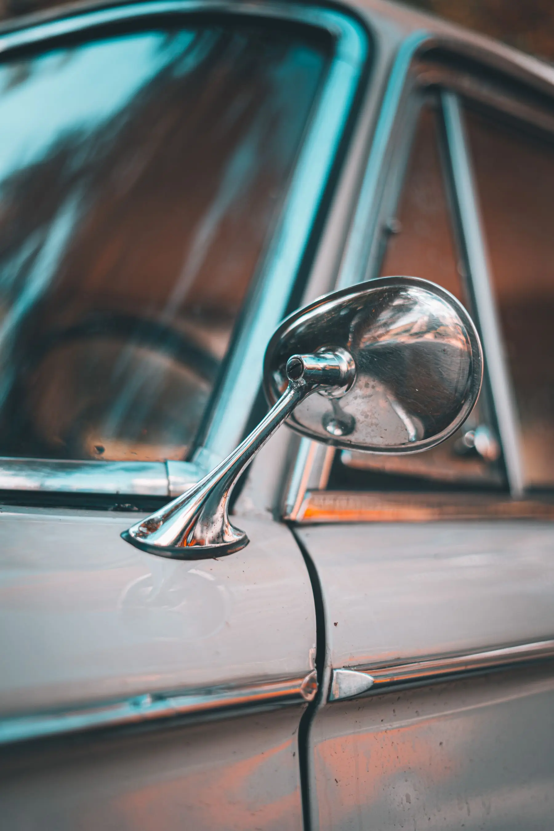 A vintage car’s rounded chrome mirror, weathered metal, and fine window trim.
