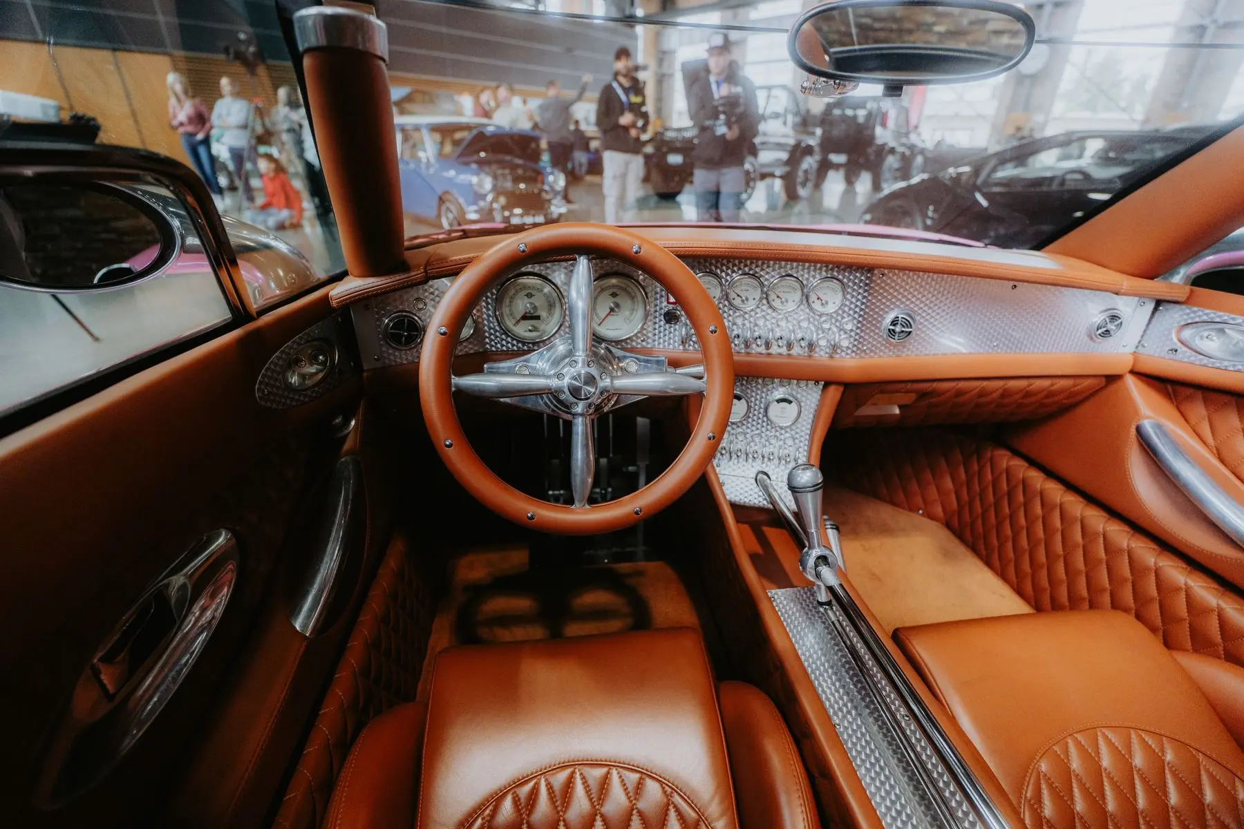 Tan quilted upholstery, a leather steering wheel, and an engine-turned metal dashboard in a classic custom car.