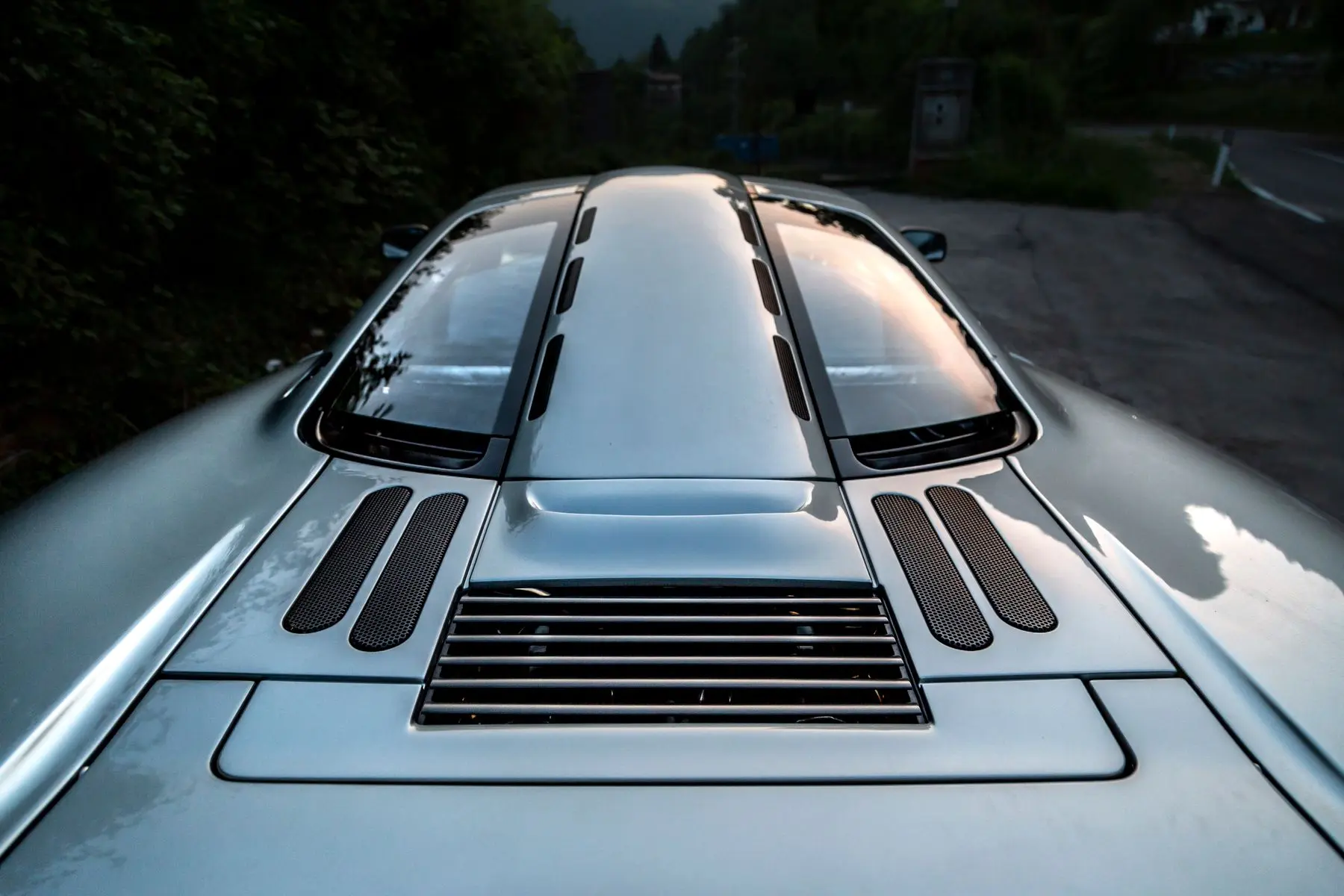 Evening sky reflected in the silver rear bodywork and glass engine cover of a supercar.