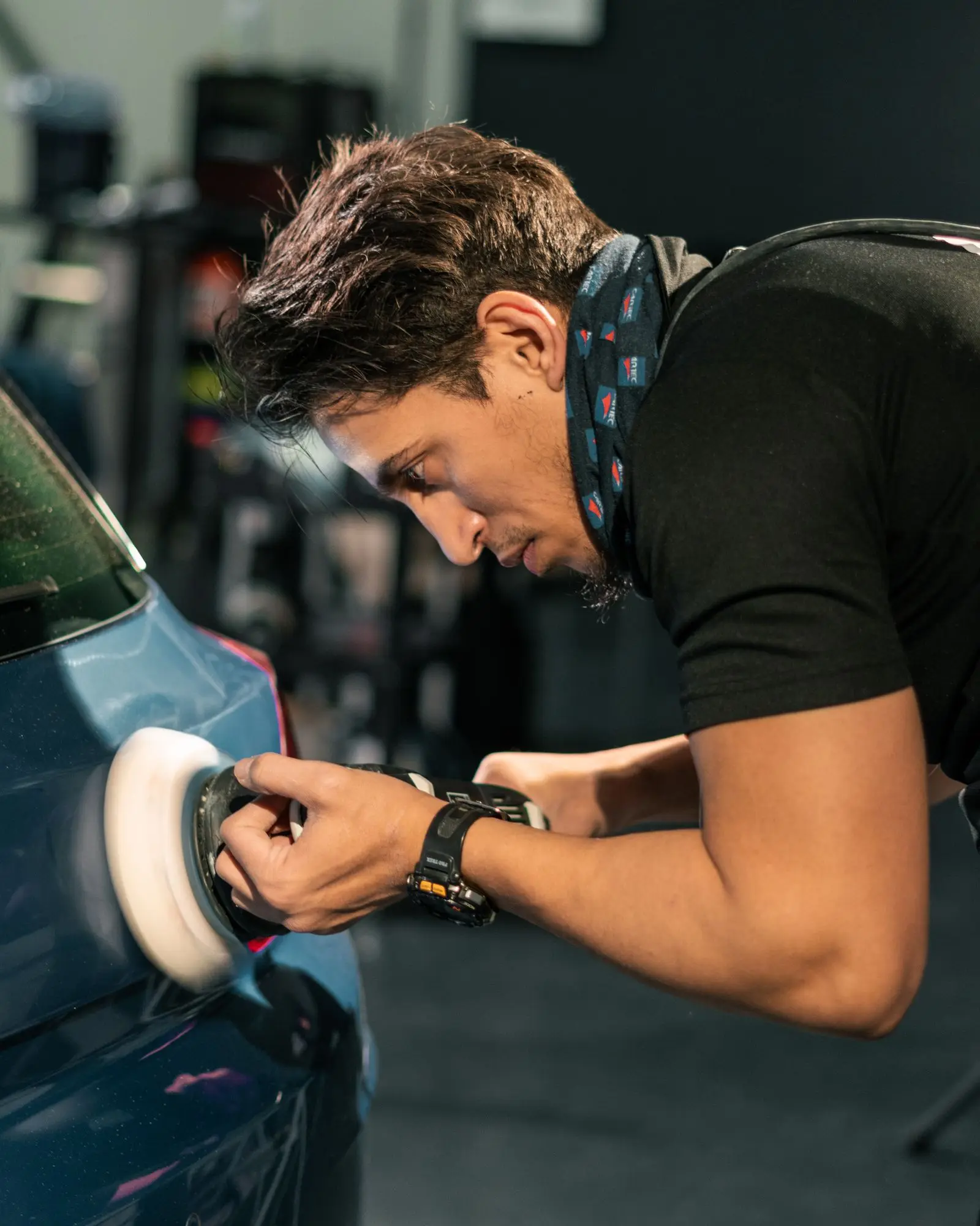 A detailer concentrating on machine polishing a car panel in a workshop.